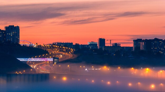 Illuminated bridge in the fog against the backdrop of sunset over the city Sunset city background