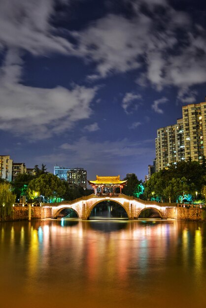 Photo illuminated bridge over river against sky in city at night