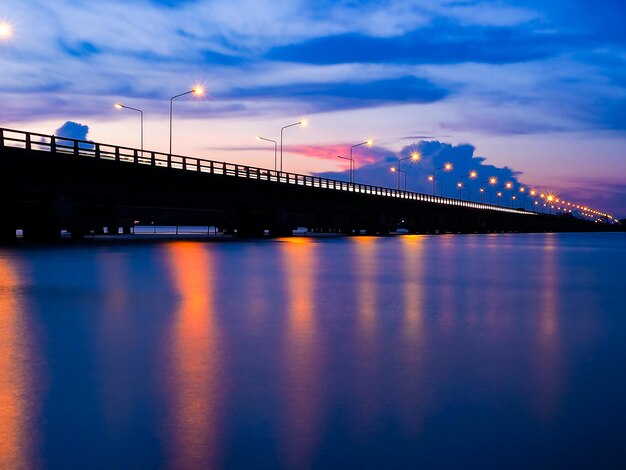 Illuminated bridge over river against sky at sunset