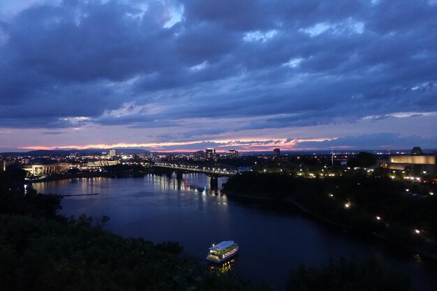 Illuminated bridge over river in city against sky at dusk