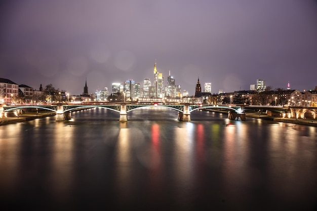 Illuminated bridge over river with buildings in background