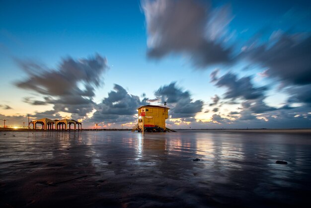 Illuminated building by sea against sky at sunset