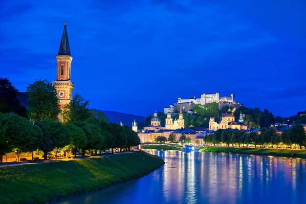 Illuminated buildings by lake against blue sky at dusk