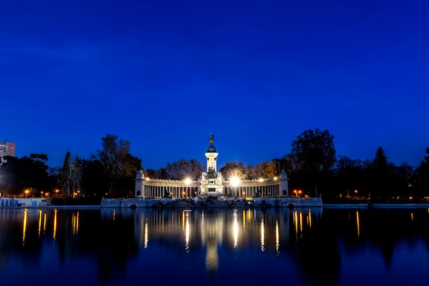 Illuminated buildings by lake against blue sky at night