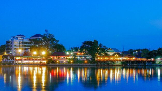 Illuminated buildings by lake against sky at night