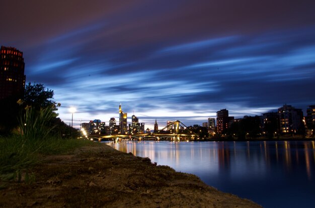 Photo illuminated buildings by river against cloudy sky