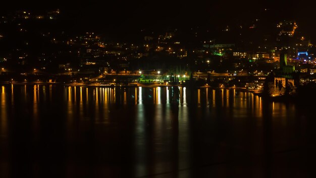 Photo illuminated buildings by river against sky at night