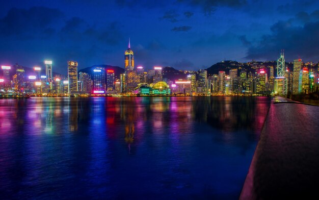 Illuminated buildings by river against sky at night