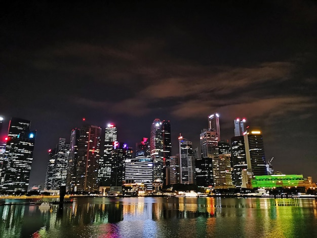 Illuminated buildings by river against sky at night