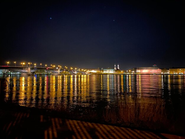 Illuminated buildings by river against sky at night