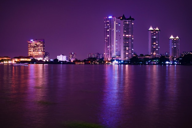 Illuminated buildings by river against sky at night