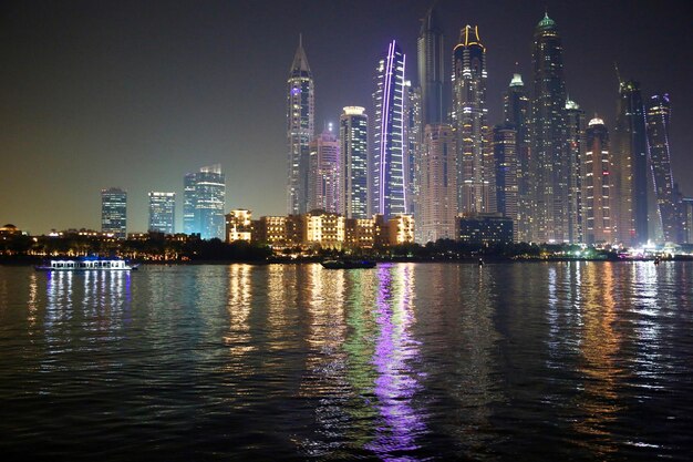 Photo illuminated buildings by river against sky at night