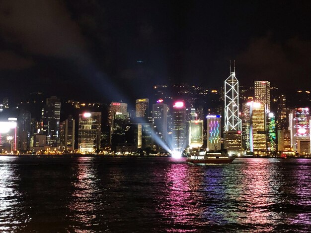 Illuminated buildings by river against sky at night