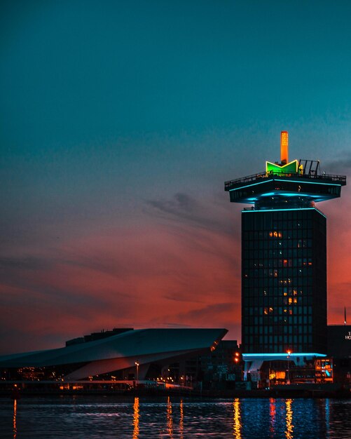 Illuminated buildings by sea against sky during sunset