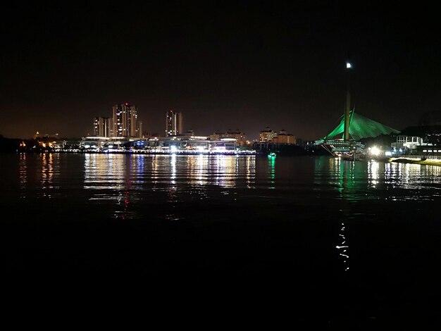 Illuminated buildings by sea against sky at night