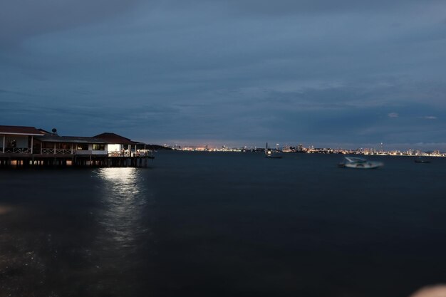 Illuminated buildings by sea against sky at night