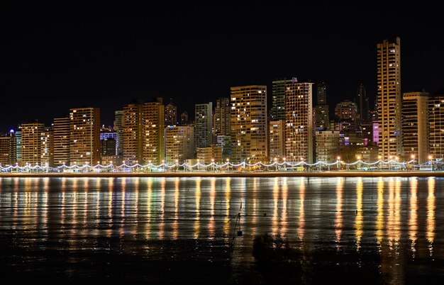 Photo illuminated buildings by sea against sky at night