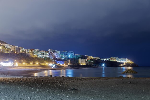 Illuminated buildings by sea against sky at night