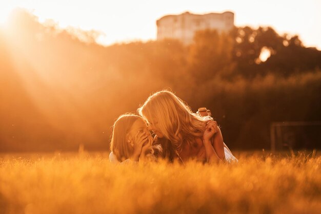 Illuminated by sunlight lying down mother with her daughter and cute dog are on the field outdoors