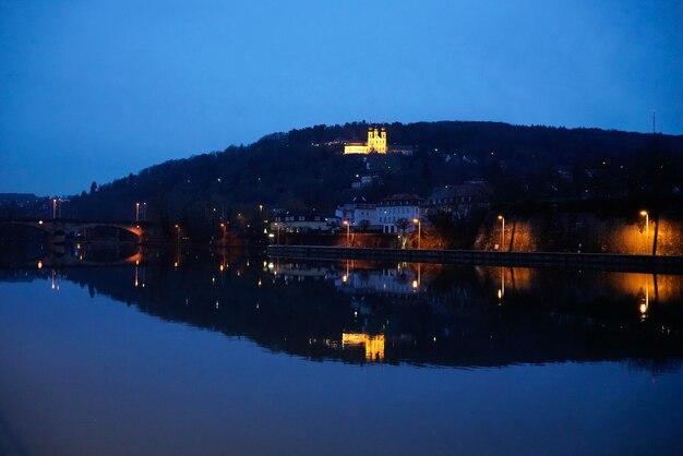 Illuminated city by lake against clear sky at night