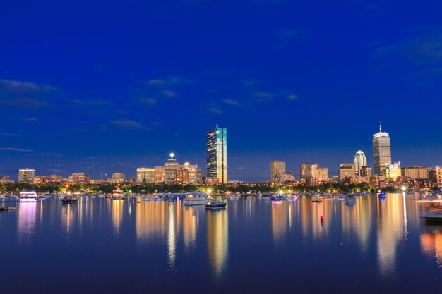 Illuminated city by river against sky at night