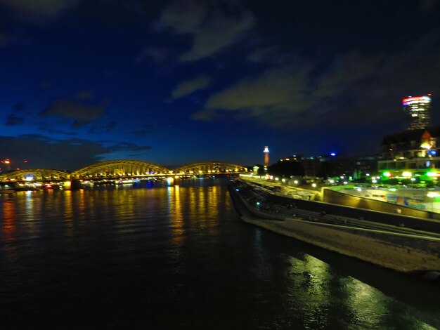 Illuminated city by river against sky at night