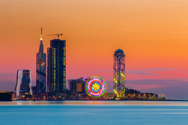 Illuminated city by river against sky during sunset