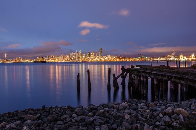 Illuminated city by sea against sky at night