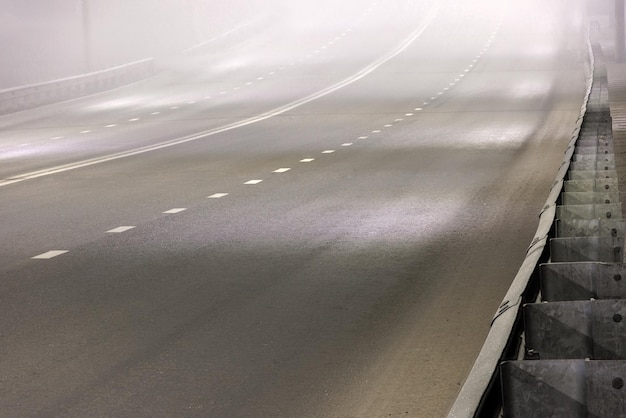 Illuminated empty foggy night road with rigid guardrails traffic barriers or crash barriers