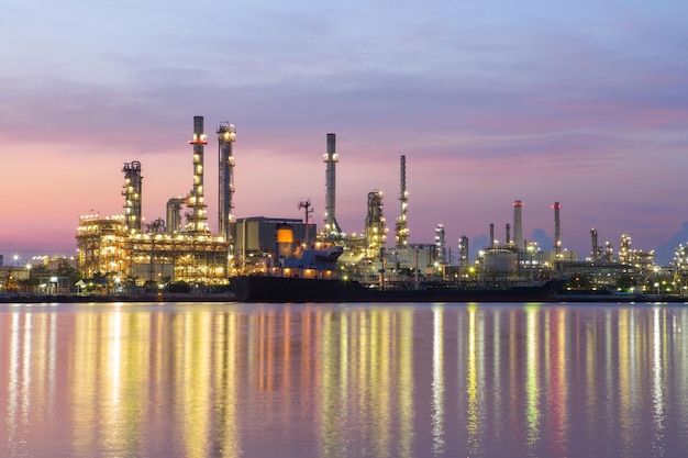 Photo illuminated factory by river against sky at dusk