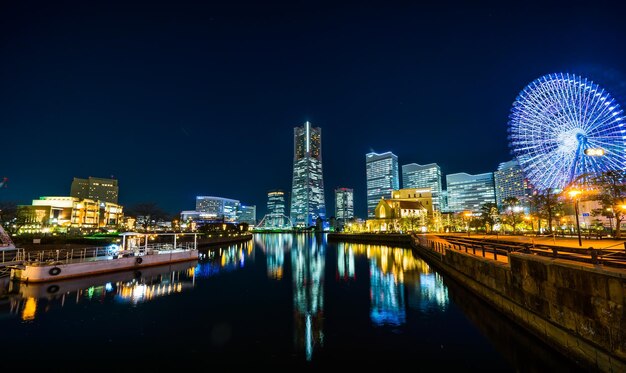 Illuminated ferris wheel by buildings against sky at night