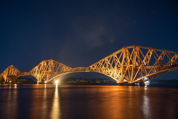 Photo illuminated firth of forth rail bridge over river at night