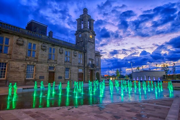 Photo illuminated human fountains outside historic building at dusk