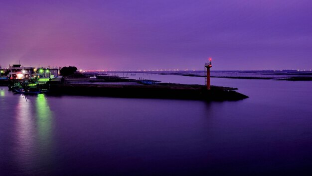 Illuminated lighthouse by sea against sky at night