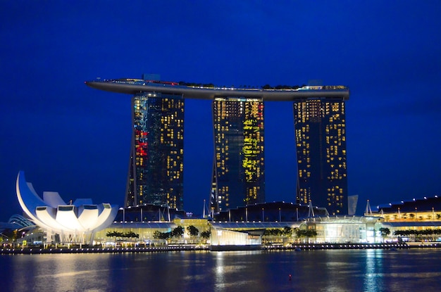 Photo illuminated marina bay sands in city by river against blue sky at night