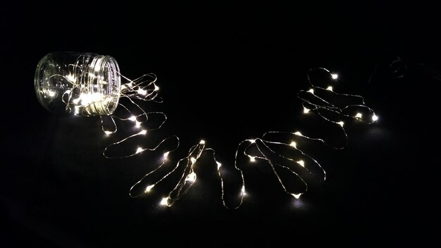 Illuminated string light and jar on black background