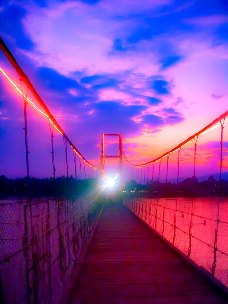 Illuminated suspension bridge against sky during sunset