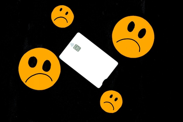 Illustration of orange paper emoticon faces cut out with sad
gesture and a white bank card on black background concept of ruin
sadness sadness dissatisfied with bank credit cards