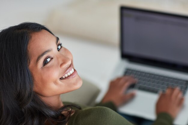 Im always connected Portrait of an attractive young woman using her laptop while sitting on the sofa at home