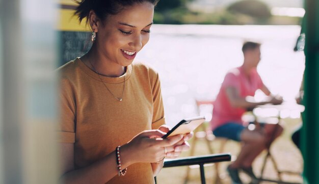 私はとても幸せです彼はついに私にメッセージを送りました彼女が彼女のスマートフォンを使用しているときに笑っている若い女性のショット