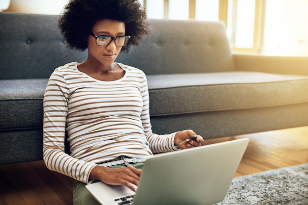 Photo im so use to paying the bills now shot of a focused young woman doing online banking with her laptop while being seated on the floor next to a couch at home