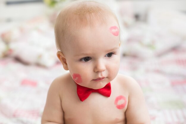 Image of adorable child with red kisses on the skin, happy boy, sitting in the Studio on the bed, angel, romantic holiday, Valentine's Day.