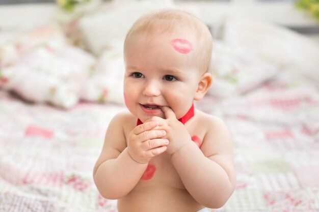 Image of adorable child with red kisses on the skin, happy boy, sitting in the Studio on the bed, angel, romantic holiday, Valentine's Day.