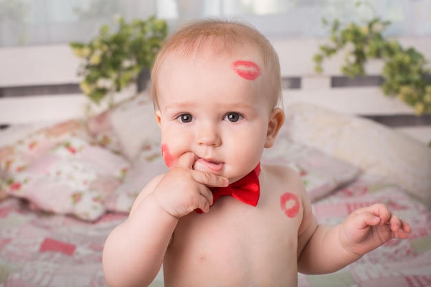 Image of adorable child with red kisses on the skin, happy boy, sitting in the Studio on the bed, angel, romantic holiday, Valentine's Day.