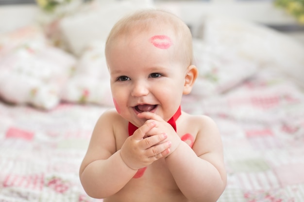 Image of adorable child with red kisses on the skin, happy boy, sitting in the Studio on the bed, angel, romantic holiday