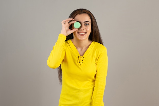 Image of adorable girl posing with colorful macaroons on gray wall.