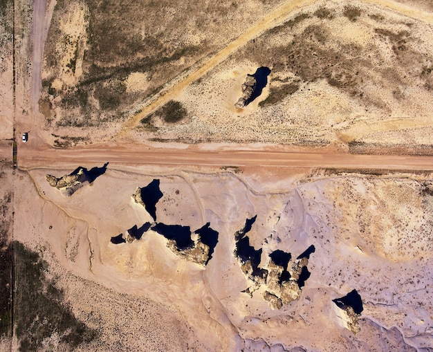 Image of Aerial view from above of desert with dirt road and obelisk rock structures with car for perspective