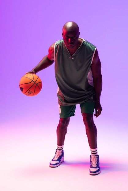 Image of african american basketball player with basketball on neon purple background. Sports and competition concept.