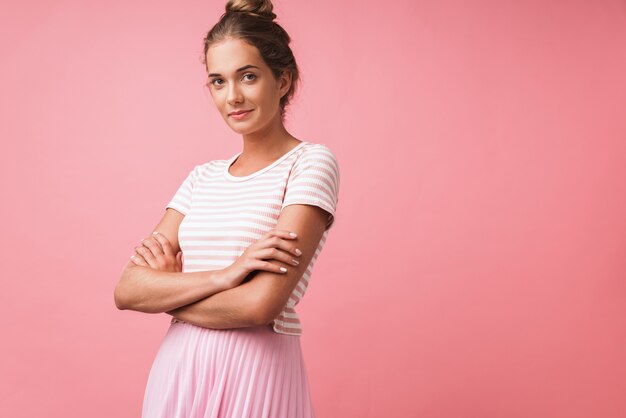 Image of alluring beautiful woman wearing striped clothes smiling and standing with arms crossed isolated over pink wall