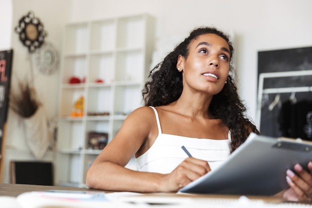 Image of amazing concentrated young business african woman in office isolated over white wall indoors work with documents writing notes.